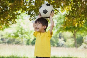 Little boy holding up football at park